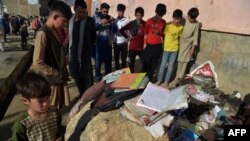 FILE - Onlookers stand next to the backpacks and books of victims the day after multiple blasts outside a girls' school in Dasht-e-Barchi on the outskirts of Kabul, May 9, 2021.