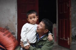FILE - Le Minh Tuan, father of the late 30-year-old Le Van Ha who was among 39 people found dead in a truck in Britain last year, holding Ha's son in their house in Vietnam's Nghe An province, Oct. 10, 2020.
