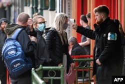 FILE - A security guard uses a handheld thermometer to take the temperature of customers, wearing face masks or coverings due to the COVID-19 pandemic, as they wait to enter a bar in Liverpool, England, Oct. 2, 2020.