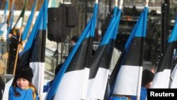 FILE - People hold national flags at the military parade during Estonia's centenary celebration in Tallinn, Feb. 24, 2018. 