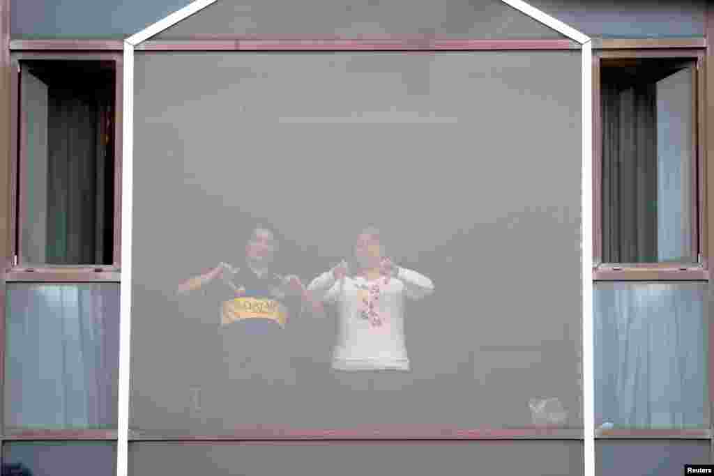 People gesture from a window at the Radisson Blu Hotel at Heathrow Airport, as Britain introduces a hotel quarantine program for arrivals from a &quot;red list&quot; of 30 countries due to the coronavirus pandemic, in London, Britain.