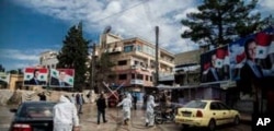 FILE - In this March 24, 2020 file photo, workers spray disinfectant to prevent the spread of the coronavirus, on a street lined with billboards showing Syrian President Bashar Assad, in Qamishli, Syria.