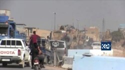 Local traffic follows as U.S. Army vehicles with flags drive down the street allegedly near the Syrian-Turkish border town Kobane, Syria, Oct. 12, 2019 in this still image taken from video.
