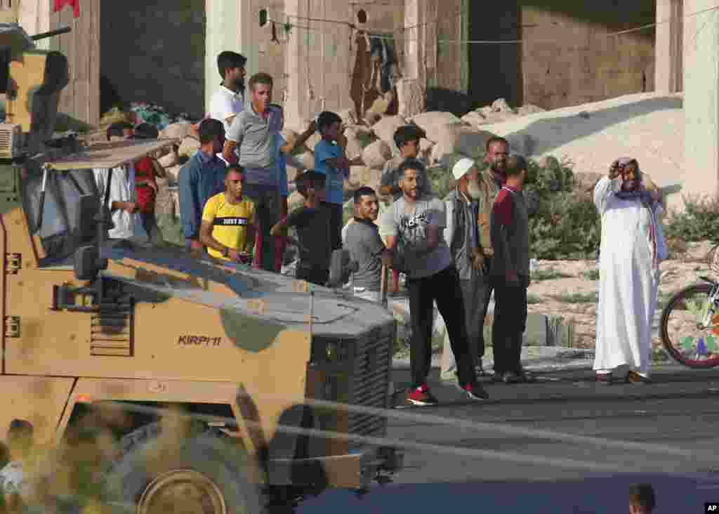 La gente observa cómo un convoy militar turco se mueve cerca de la frontera, poco después del inicio de una operación turca dentro de Siria. (Foto AP / Lefteris Pitarakis).