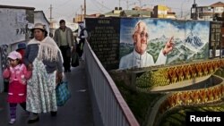 Residentes de El Alto, Bolivia, caminan frente a un mural alusivo a la visita del Papa a Ecuador, Bolivia y Paraguay.