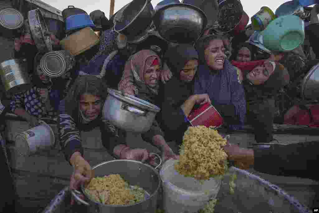 Palestinian girls struggle as they get donated food at a distribution center in Khan Younis, Gaza Strip.