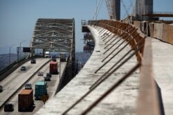 FILE - Traffic moves on the old Gerald Desmond Bridge next to its replacement bridge under construction in Long Beach, Calif., July 2, 2018. President Donald Trump's tariffs provoke retaliatory tariffs on U.S. exports.