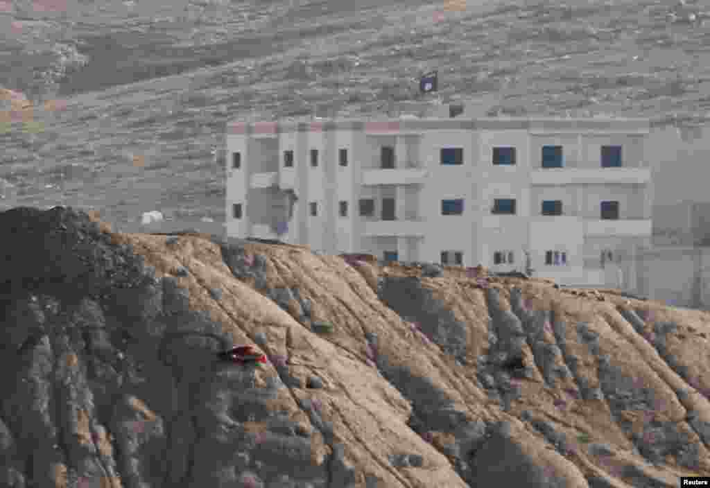 A black flag belonging to the Islamic State flies from the roof of a building in Kobani, Syria, Oct. 6, 2014.