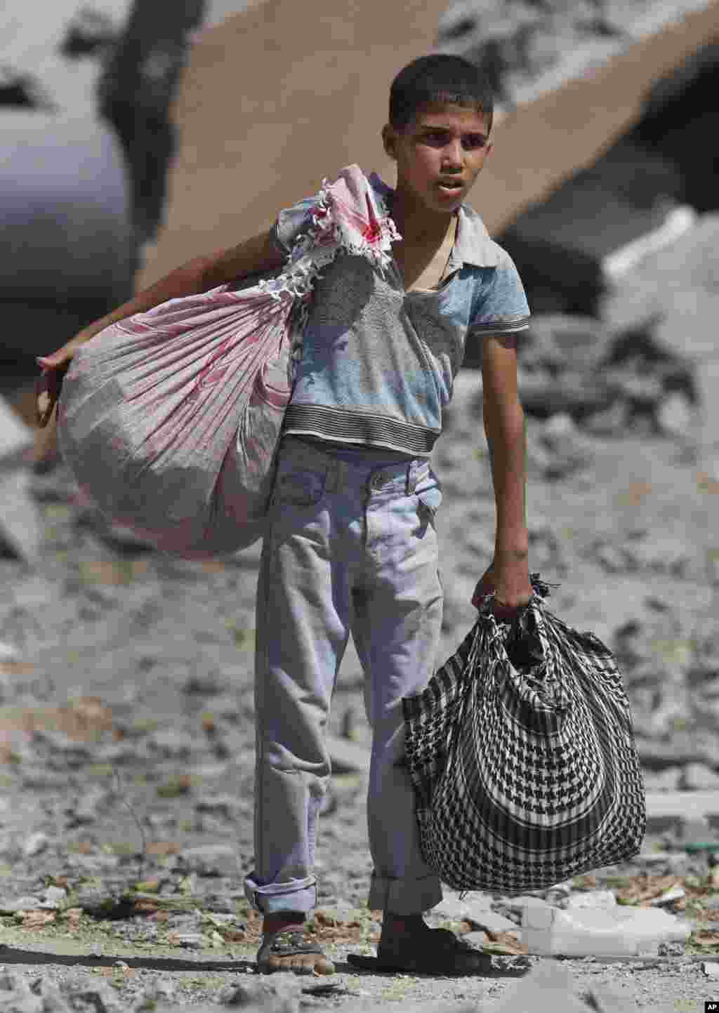 A Palestinian boy carries his belongings after salvaging them from his destroyed house, in the heavily bombed town of Beit Hanoun, Gaza Strip, close to the Israeli border, Aug. 1, 2014.