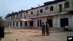 In this photo taken with a mobile phone, soldiers stand outside a burnt out shopping mall in Maiduguri, Nigeria, October 8, 2012.