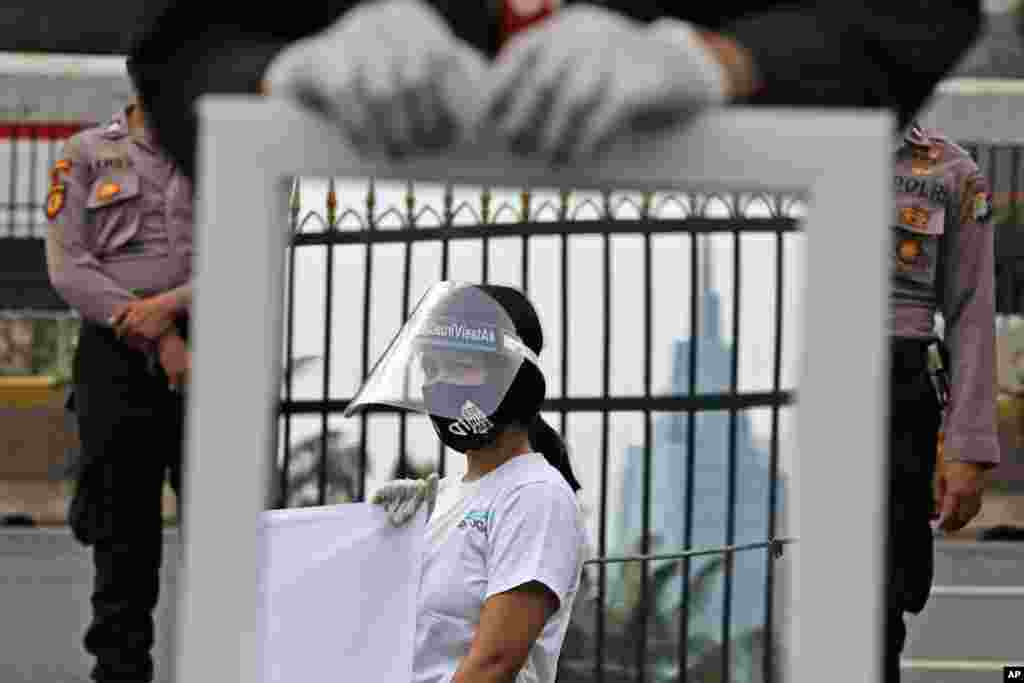 A mirror reflects an activist wearing a mask and protective face shield as a precaution against the new coronavirus outbreak during a small protest outside the parliament in Jakarta, Indonesia.