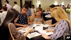 FILE - people fill out job applications at a job fair, in Miami Lakes, Fla.