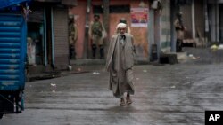 A Kashmiri man walks as Indian paramilitary soldiers stand guard during security lockdown in Srinagar, Indian controlled Kashmir, Wednesday, Aug. 14, 2019.