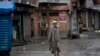 Seorang pria Kashmir berjalan di tengah jalanan yang sepi, di Srinagar, kawasan Kashmir yang dikuasai oleh India, diawasi oleh para penjaga keamanan, 14 Agustus 2019. 