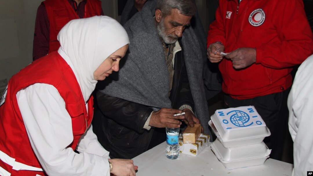 Para anggota organisasi Bulan Sabit Merah berseragam merah memberi makanan dan minuman pada seorang pria sebelum ia naik bus untuk dievakuasi dari Homs, Suriah (7/2).