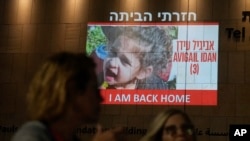 2023年11月26日，人们走过特拉维夫一栋大楼上投射出的4岁阿比盖尔·伊丹(Abigail Edan)的照片，她是哈马斯扣押的人质，于周日前夕被释放。伊丹的父母均被哈马斯武装分子杀害。10月7日，她遭到绑架，这是一次跨境袭击，促使以色列向哈马斯宣战。 （美联社照片）