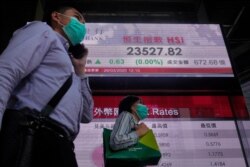 People wearing face masks walk past a bank electronic board showing the Hong Kong share index at Hong Kong Stock Exchange, March 26, 2020.