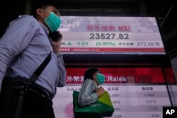 People wearing face masks walk past a bank electronic board showing the Hong Kong share index at Hong Kong Stock Exchange, March 26, 2020.