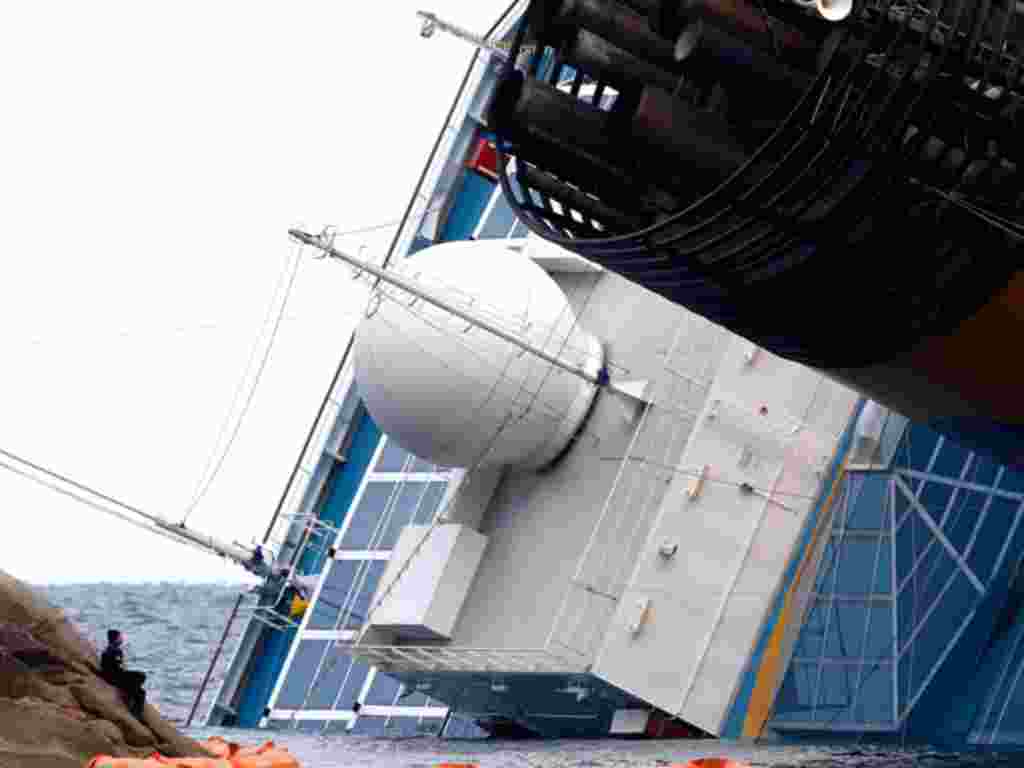 Seorang penyelam (kiri) beristirahat sambil memandangi kapal pesiar Costa Concordia di hadapannya (Reuters).