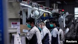 FILE - Employees wearing face masks work on a car seat assembly line at Yanfeng Adient factory in Shanghai, China, Feb. 24, 2020. 