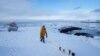 Seorang wanita membawa dua anjingnya berjalan-jalan menyusuri pantai di kota Nuuk, Greenland. (AP)<br />
&nbsp;