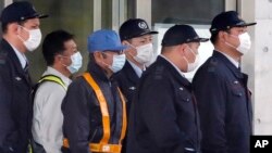 A masked man, third from left with blue cap, believed to be former Nissan Chairman Carlos Ghosn, walks out with security guards from Tokyo Detention Center in Tokyo, March 6, 2019, after posting 1 billion yen ($8.9 million) in bail.