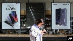 FILE - A woman checks her phone as she walks by posters adverting smartphones at a mobile phone store in Seoul, South Korea, Oct. 17, 2017.