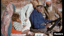 An undated photo released Oct. 14, 2017, shows family members watching Australia's most famous Aboriginal artist, Albert Namatjira, sitting on a rock as he paints.