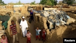 FILE - An internally displaced Sudanese family poses for a photograph outside their makeshift shelter within the Kalma camp for internally displaced persons (IDPs) in Darfur.