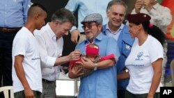 El presidente de Colombia, Juan Manuel Santos (segundo desde la izquierda) y el principal comandante de las FARC, Rodrigo Londoño, alias Timoleón Jiménez o Timochenko (tercero desde la derecha) saludan al bebé de ua pareja rebelde en un acto para conmemorar el fin del desarme, en Buenavista, Colombia, el martes, 27 de junio de 2017.