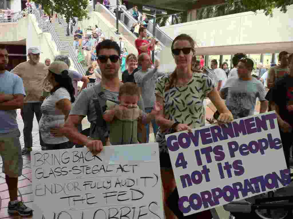 Una pareja con su hijo de meses muestran los letreros que hicieron para la protesta a las afueras de la alcaldía de la ciudad de Miami.