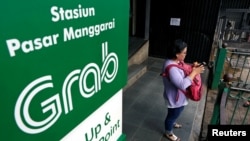 Seorang perempuan sedang menggunakan ponselnya dekat tanda layanan transportasi online Grab di Stasiun Kereta Manggarai, Jakarta, 3 Juli 2019. (Foto: Reuters)