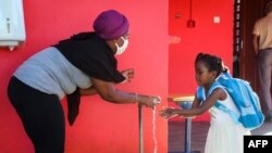 FILE - A staff member, wearing a protective facemask, helps a student to wash her hands at Malamani Primary School, in Chirongui, on the French Indian Ocean island of Mayotte, May 27, 2020.