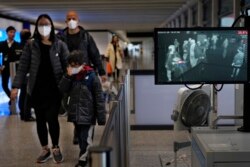FILE - A health surveillance officer uses a temperature scanner to monitor passengers arriving at Hong Kong International Airport in Hong Kong, Jan. 25, 2020.