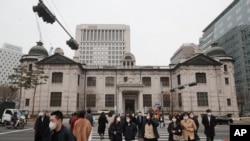 People wearing face masks walk by the headquarters of the Bank of Korea in Seoul, South Korea, March 4, 2021. South Korea's central bank says the country's economy shrank for the first time in 22 years in 2020. 