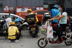 A woman wearing a face mask rides an electric bicycle with her groceries past delivery workers of Meituan and Ele.me, in Beijing, China, July 13, 2020.