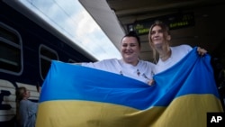 La rapera ucraniana alyona alyona, izquierda, y la cantante Jerry Heil posan para medios con la bandera ucraniana antes de partir en una estación de tren en Kiev, Ucrania, el 25 de abril de 2024. El dúo representará a Ucrania en el festival Eurovisión en Malmö, Suecia.