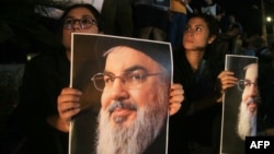 Des manifestants tiennent des photos de Hassan Nasrallah, chef défunt du groupe libanais Hezbollah, lors d'une veillée de protestation dans la ville de Sidon, dans le sud du Liban, le 28 septembre 2024. (Photo de Mahmoud ZAYYAT / AFP)