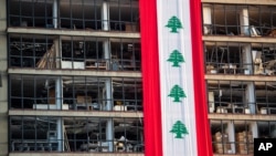 A banner with representations of the Lebanese flag hangs on a damaged building in a neighborhood near the site of last week's explosion that hit the seaport of Beirut, Lebanon, Wednesday, Aug. 12, 2020. 