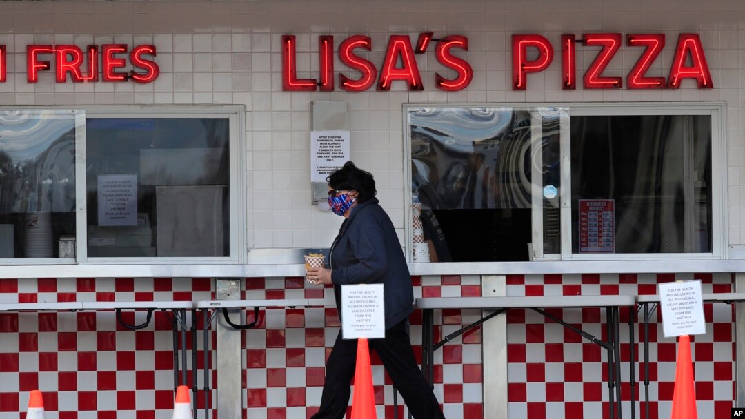 In this May 7, 2020 photo, a customer leaves the sidewalk window with her French fries at Lisa's Pizza in Old Orchard Beach, Maine, one of the few in the tourist town that have reopened during the coronavirus pandemic.