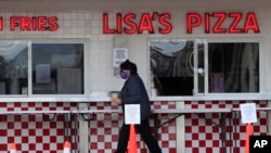 In this May 7, 2020 photo, a customer leaves the sidewalk window with her French fries at Lisa's Pizza in Old Orchard Beach, Maine, one of the few in the tourist town that have reopened during the coronavirus pandemic.