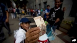 Seorang pedagang memeriksa keaslian uang kertas lembaran 100 bolivar, sementara warga antri untuk menukar uang di sebuah bank di Caracas, Venezuela, 13 Desember 2016. (AP Photo/Fernando Llano)