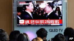 Personas observan una pantalla de TV mientras el ministro de Unificación de Corea del Sur (izquierda) saluda a su contraparte del Norte.