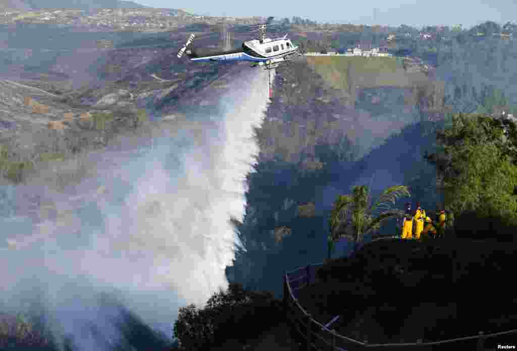 A helicopter drops water on a burning hillside next to homes as firefighters battle the Bernardo Fire, north of San Diego, California, May 13, 2014. More than 20,000 homes and other residences were being evacuated in and around San Diego as a fast-moving, fire and county officials said.