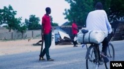 A cyclist rides past Civilian Joint Force members who are patrolling the streets looking for Boko Haram fighters. Maiduguri, Nigeria. (C. Oduah for VOA)