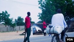 Un cycliste roule sur son vélo à côté des membres de la Force conjointe civile qui patrouillent dans les rues à la recherche de combattants de Boko Haram, à Maiduguri, Nigeria, juin 2016. (C. Oduah pour VOA)