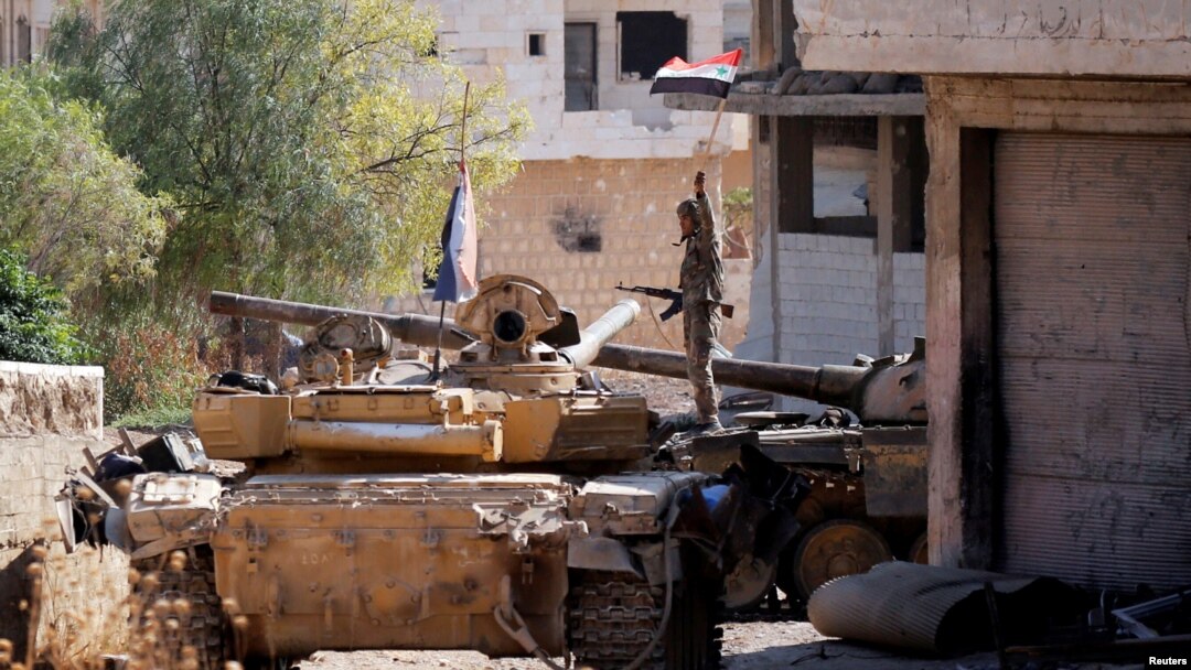 Seorang prajurit tentara Suriah memegang bendera Suriah ketika ia berdiri di atas kendaraan militer di Khan Sheikhoun, Idlib, Suriah, 24 Agustus 2019. (Foto: Reuters)