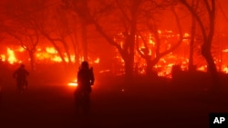 ILUSTRASI -Dua orang mengendarai sepeda motor saat Kebakaran Palisades menghancurkan sebuah area di kawasan Pacific Palisades, Los Angeles, pada 7 Januari 2025. (Etienne Laurent/AP)