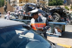 FILE - A policeman passes out leaflets with road accident statistics, in front of a destroyed car which is put on display, during a campaign to promote safe driving in Beirut, April 25, 2007.