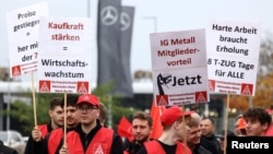 Protesters hold up signs during a protest rally by employees of German carmaker Mercedes demanding higher wages, at a Mercedes plant in Berlin, Germany, Oct. 29, 2024.